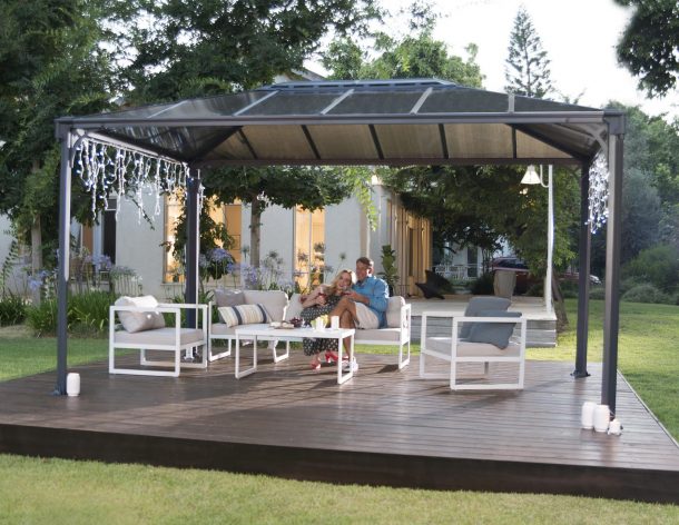An aluminum gazebo 10'x14' with polycarbonate roof on a deck patio is used by a couple for relaxation